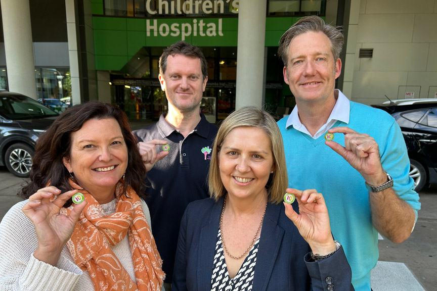 Two ladies and two men smiling and holding their 10 years of services badges, outside the Queensland Children's Hospital