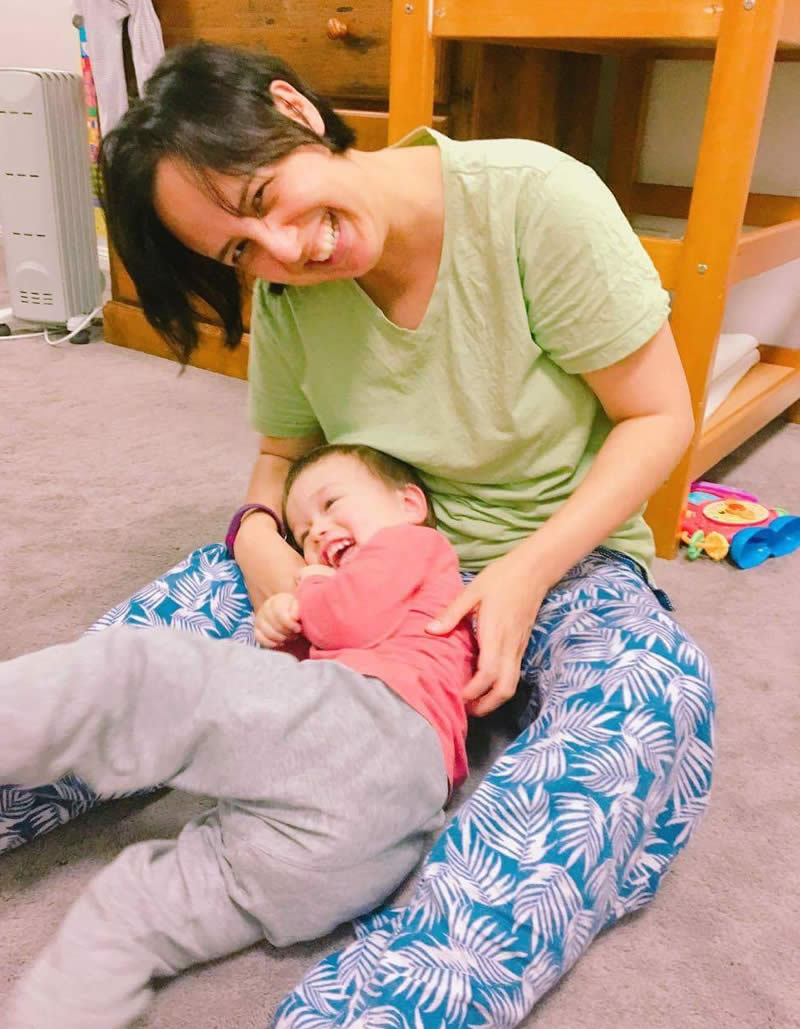 A smiling woman is holding a little boy in her lap while sitting on the floor.